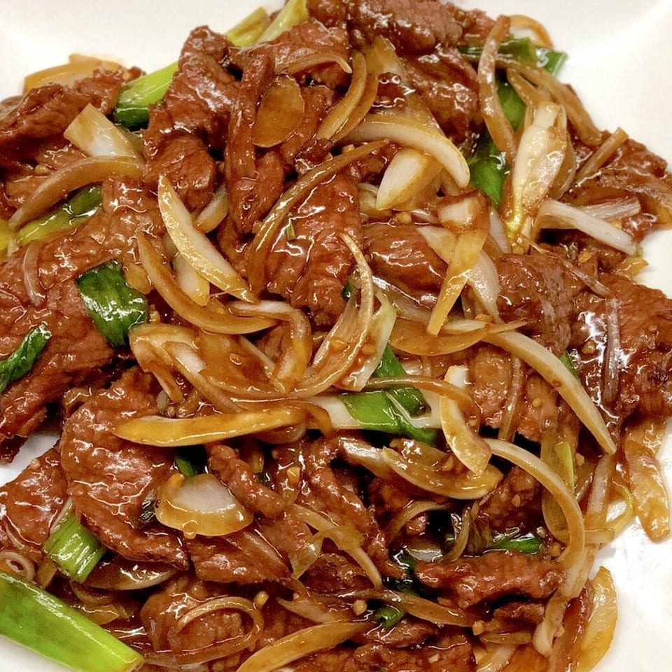 Close-up of Vietnamese stir-fried beef with onions and green scallions in a savory sauce.