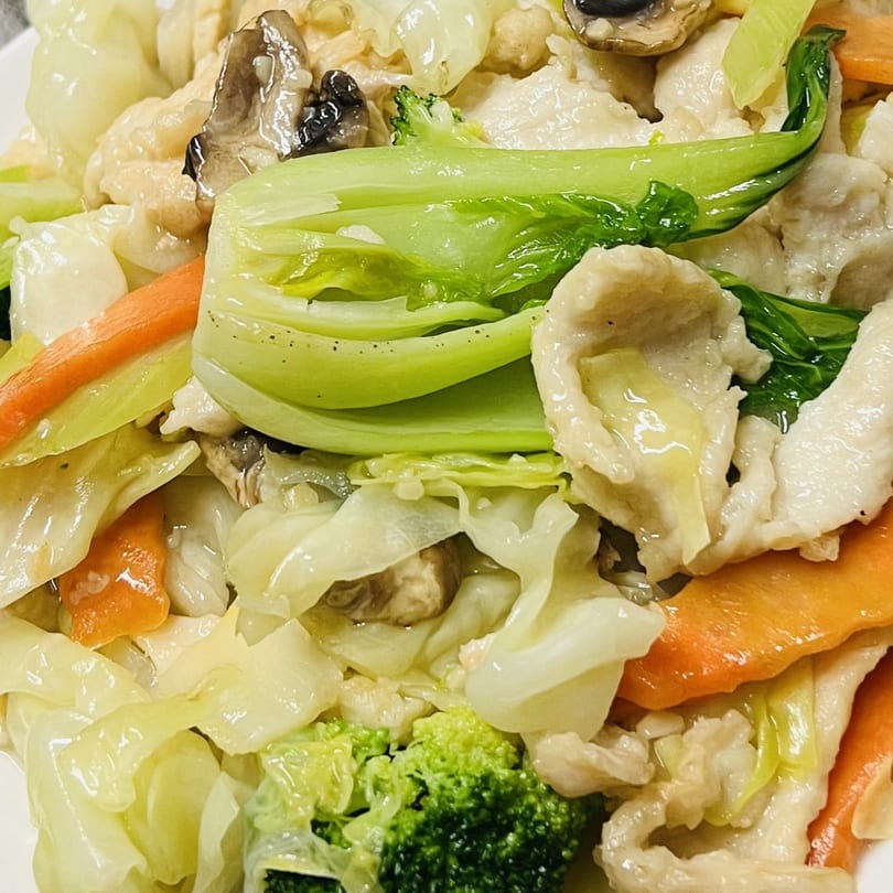 Close-up of a Vietnamese stir-fry with chicken, bok choy, carrots, broccoli, and mushrooms.