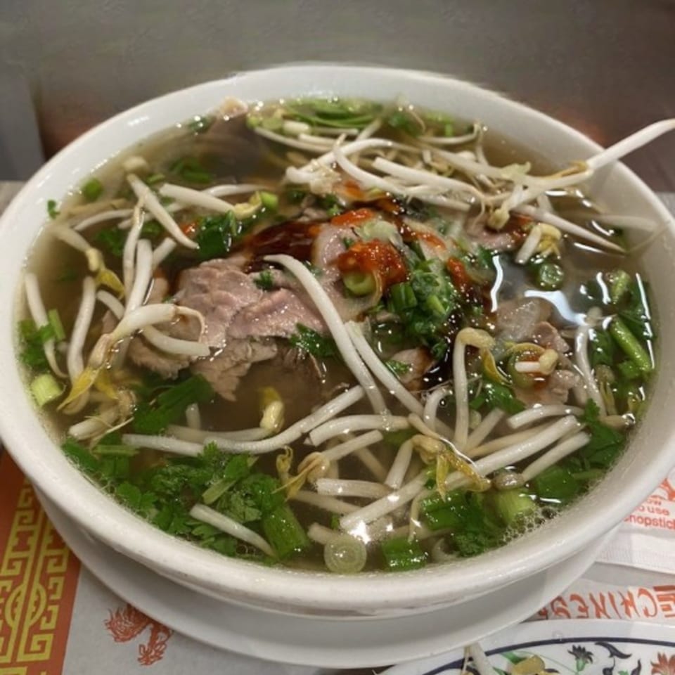 A bowl of Golden Pho's Vietnamese pho with beef, bean sprouts, and herbs, topped with sriracha.
